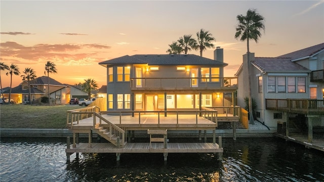 back house at dusk featuring a water view, a balcony, and a yard