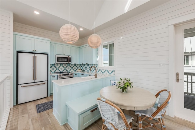 kitchen with hanging light fixtures, appliances with stainless steel finishes, light wood-type flooring, and kitchen peninsula