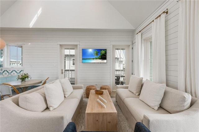 living room featuring a wealth of natural light, high vaulted ceiling, and wood walls