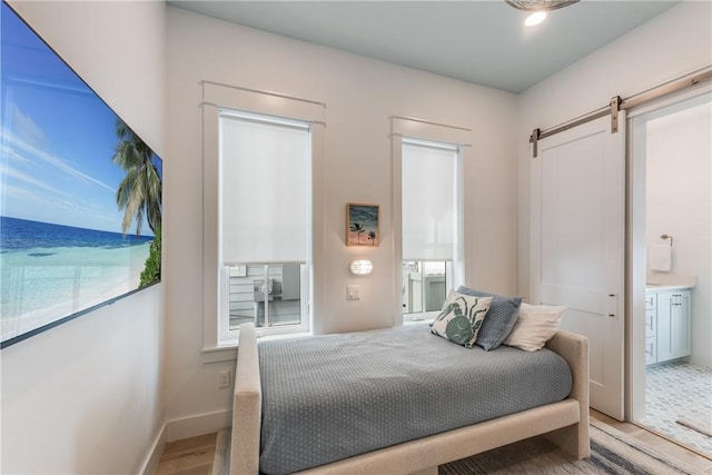 bedroom with connected bathroom, wood-type flooring, and a barn door