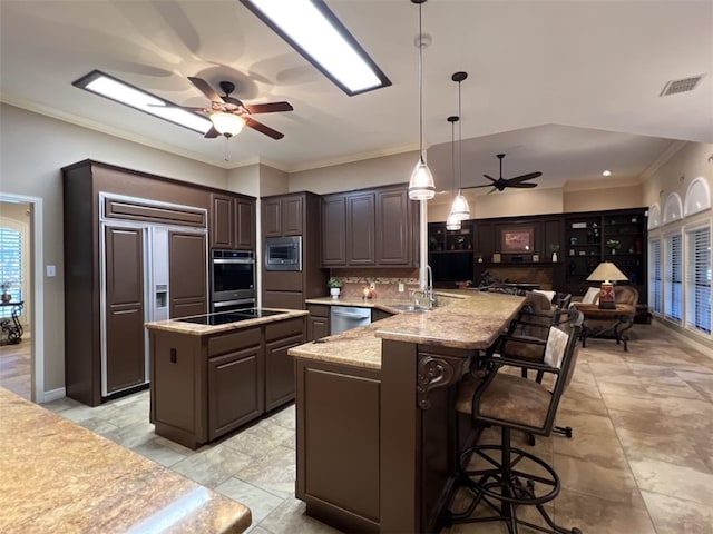 kitchen with a center island with sink, dark brown cabinets, built in appliances, hanging light fixtures, and sink