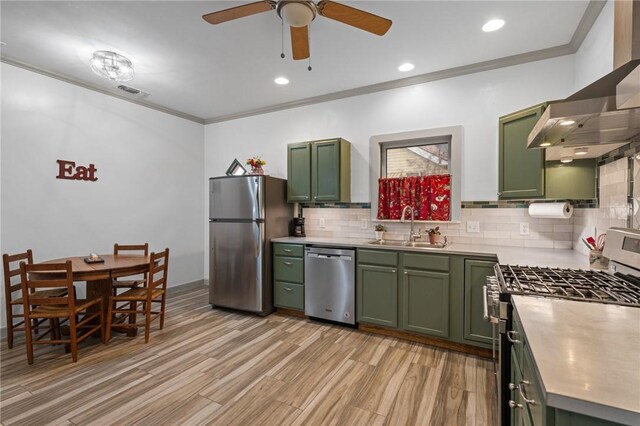 kitchen with a sink, wall chimney range hood, appliances with stainless steel finishes, and green cabinetry