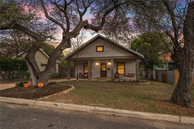 bungalow featuring a porch, a front yard, and fence