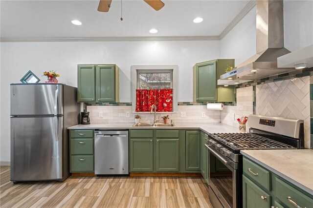 kitchen with green cabinetry, appliances with stainless steel finishes, a sink, and wall chimney range hood