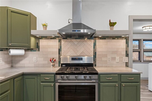 kitchen with tasteful backsplash, green cabinets, stainless steel range with gas stovetop, light countertops, and island exhaust hood