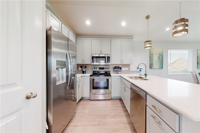 kitchen featuring stainless steel appliances, sink, tasteful backsplash, pendant lighting, and light hardwood / wood-style flooring