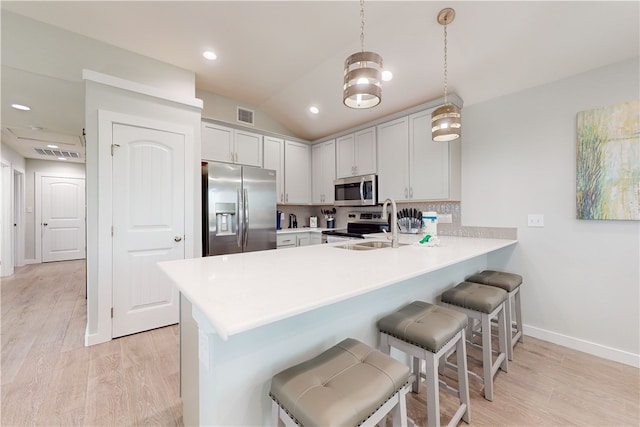 kitchen with a kitchen bar, stainless steel appliances, vaulted ceiling, kitchen peninsula, and pendant lighting