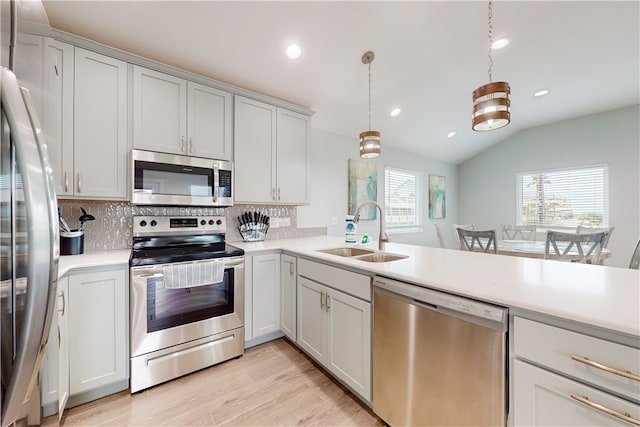 kitchen with stainless steel appliances, sink, decorative light fixtures, light hardwood / wood-style flooring, and vaulted ceiling