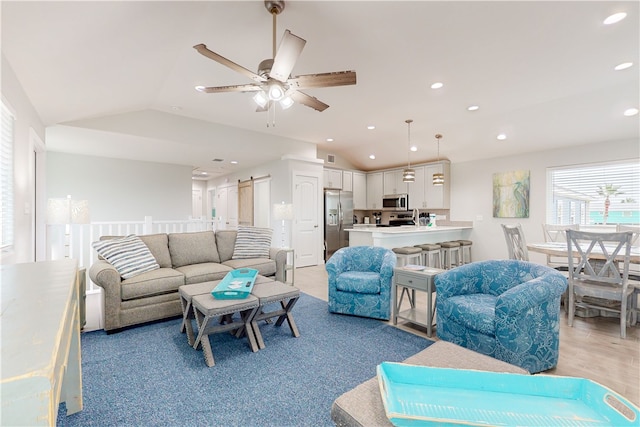 living room with a barn door, ceiling fan, and vaulted ceiling