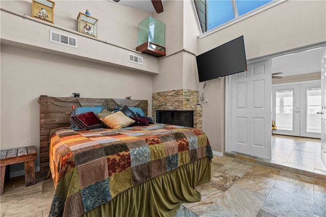 bedroom featuring a stone fireplace, french doors, a towering ceiling, and ceiling fan