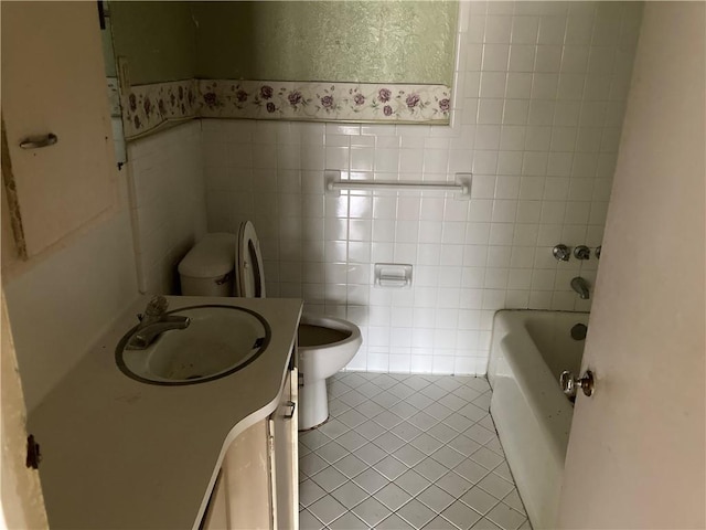 bathroom with toilet, vanity, tile walls, tile patterned floors, and a bath