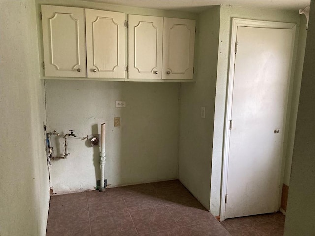 clothes washing area with dark tile patterned floors and cabinets