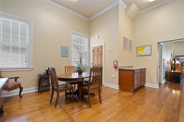 dining space with plenty of natural light, ornamental molding, a high ceiling, and light wood-type flooring