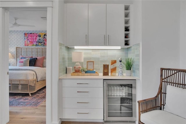 bar with decorative backsplash, white cabinetry, light hardwood / wood-style flooring, and beverage cooler