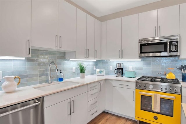 kitchen with white cabinetry, sink, light hardwood / wood-style flooring, decorative backsplash, and appliances with stainless steel finishes