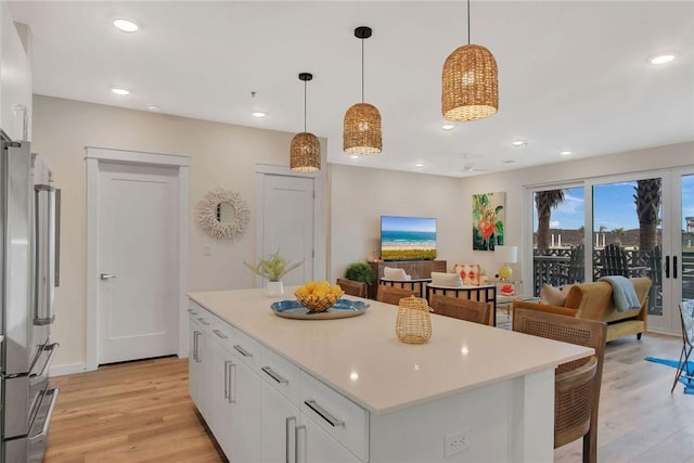 kitchen featuring a kitchen island, decorative light fixtures, white cabinets, light hardwood / wood-style floors, and stainless steel refrigerator