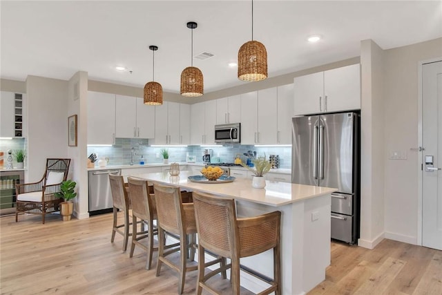 kitchen featuring hanging light fixtures, white cabinets, light wood-type flooring, and appliances with stainless steel finishes