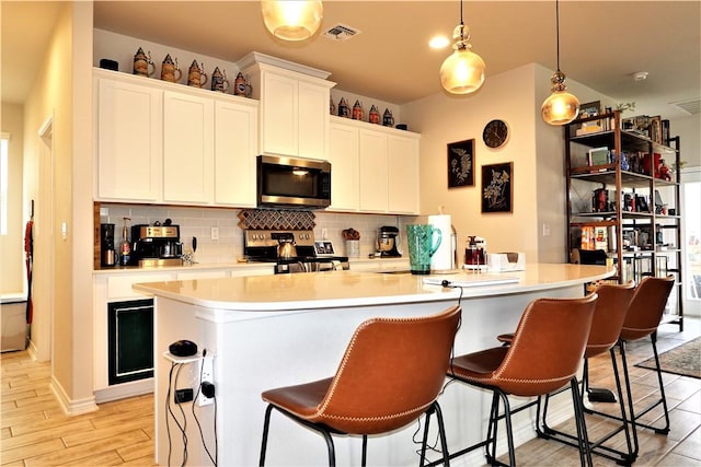 kitchen featuring an island with sink, white cabinets, hanging light fixtures, stainless steel appliances, and light wood-type flooring