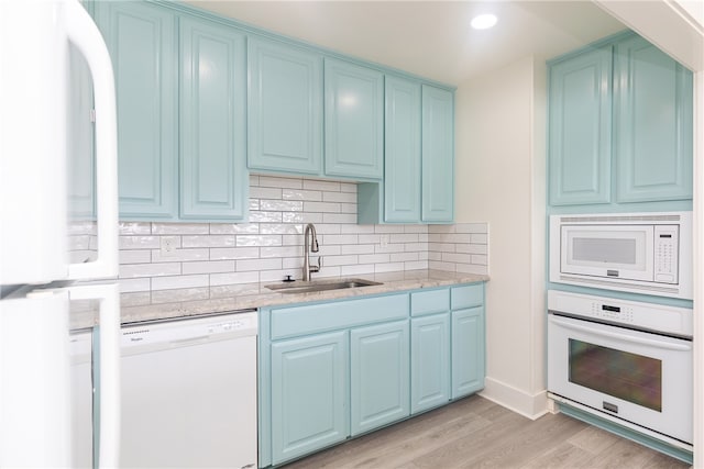 kitchen featuring sink, light stone countertops, white appliances, light hardwood / wood-style flooring, and decorative backsplash