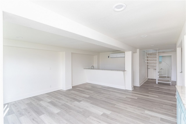 unfurnished living room featuring a wall mounted AC and light hardwood / wood-style flooring