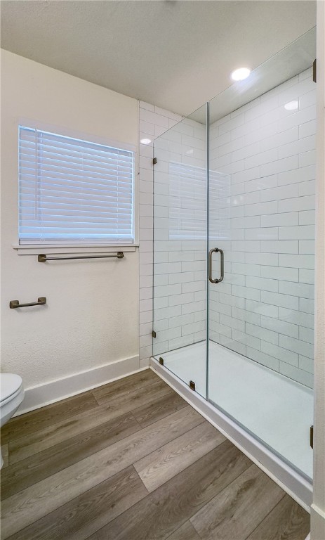 bathroom with toilet, wood-type flooring, and a shower with shower door