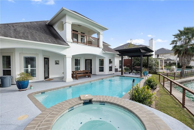 rear view of house featuring a balcony, fence, a pool with connected hot tub, stucco siding, and a patio area