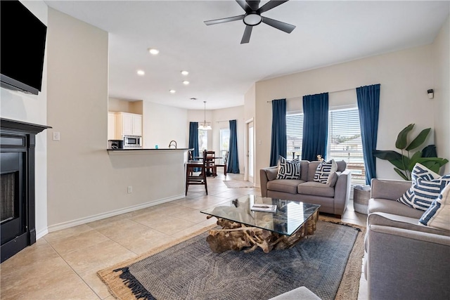 living area featuring light tile patterned floors, ceiling fan, a fireplace, and baseboards