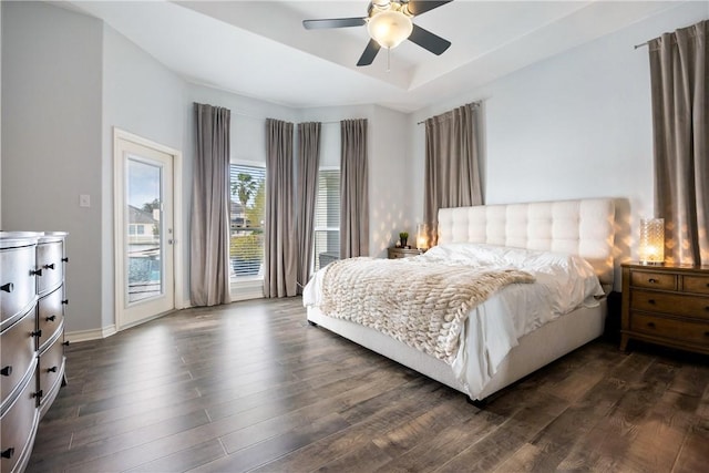 bedroom with dark wood-style floors, access to outside, a tray ceiling, and a ceiling fan