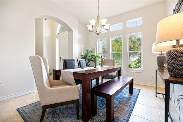 dining space featuring light tile patterned floors, an inviting chandelier, arched walkways, and baseboards