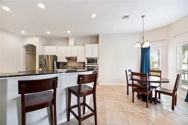 kitchen with arched walkways, visible vents, appliances with stainless steel finishes, backsplash, and dark countertops