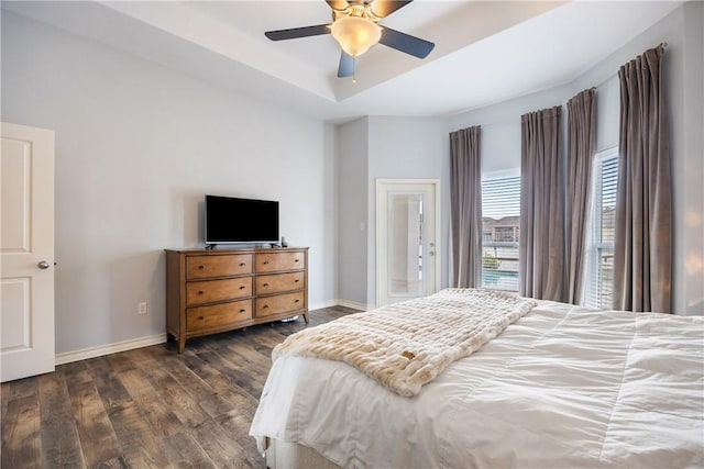 bedroom with a ceiling fan, a tray ceiling, baseboards, and wood finished floors