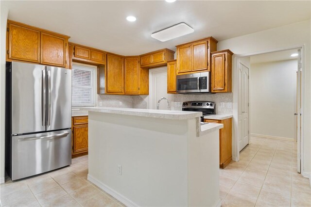 kitchen with decorative backsplash, light countertops, stainless steel appliances, brown cabinetry, and light tile patterned floors