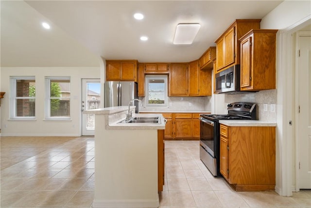 kitchen with tasteful backsplash, stainless steel appliances, a sink, a kitchen island with sink, and brown cabinetry