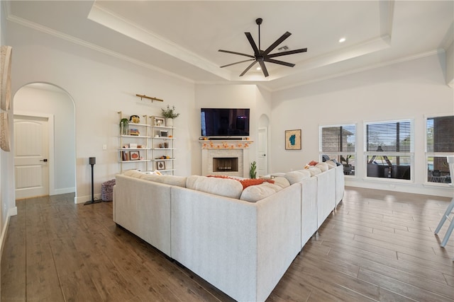 living area with a fireplace, arched walkways, a raised ceiling, and dark wood-type flooring