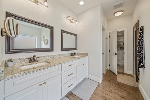 full bath with double vanity, wood finished floors, a sink, and visible vents