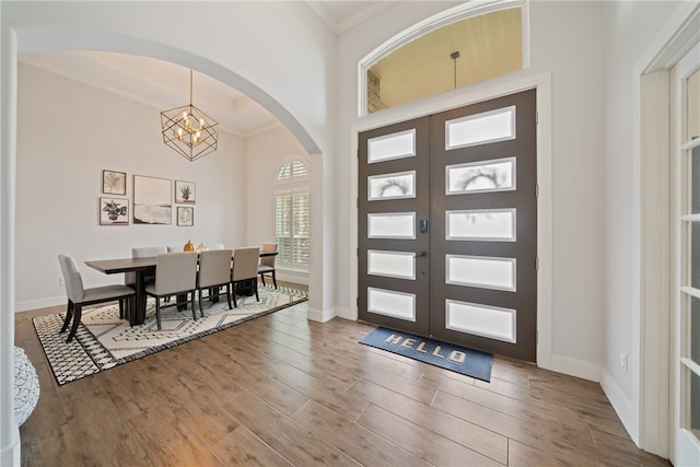 foyer entrance featuring arched walkways, ornamental molding, wood finished floors, a chandelier, and baseboards