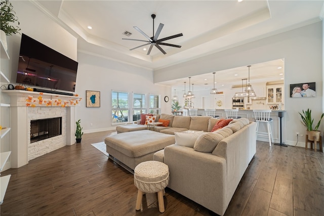 living room with a fireplace, a raised ceiling, dark wood finished floors, and a ceiling fan