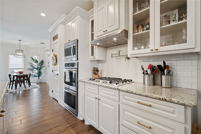 kitchen with appliances with stainless steel finishes, glass insert cabinets, white cabinetry, light stone countertops, and under cabinet range hood