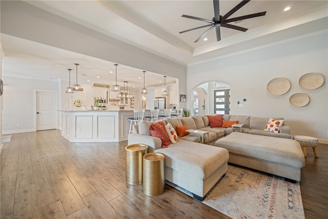 living room featuring ornamental molding, light wood-type flooring, arched walkways, and a tray ceiling