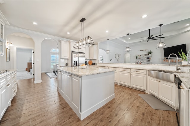 kitchen featuring stainless steel fridge, arched walkways, white cabinets, hanging light fixtures, and a sink