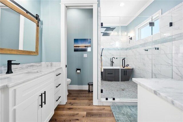 bedroom featuring connected bathroom, ornamental molding, ceiling fan, a barn door, and dark wood-type flooring