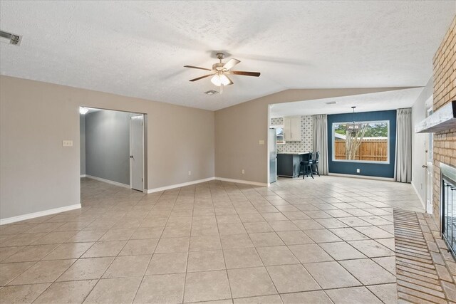 unfurnished living room with a textured ceiling, lofted ceiling, a fireplace, light tile patterned floors, and ceiling fan with notable chandelier