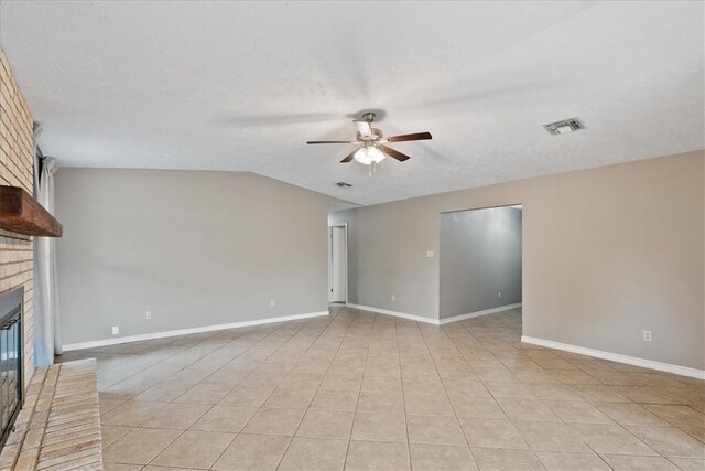 unfurnished living room with ceiling fan, light tile patterned flooring, a textured ceiling, and a brick fireplace