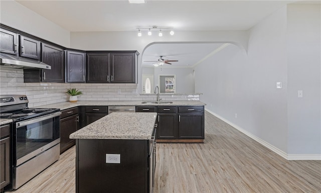 kitchen featuring arched walkways, stainless steel appliances, a sink, and under cabinet range hood