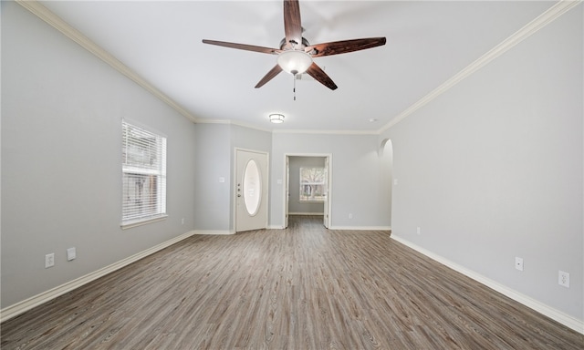 unfurnished living room featuring a wealth of natural light, crown molding, baseboards, and wood finished floors