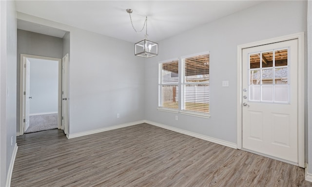 unfurnished dining area with a chandelier, baseboards, and wood finished floors