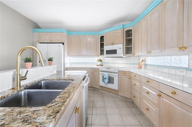 kitchen with white appliances, a sink, light brown cabinetry, glass insert cabinets, and decorative backsplash