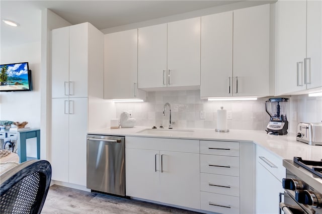 kitchen featuring stainless steel appliances, white cabinetry, decorative backsplash, sink, and light hardwood / wood-style flooring