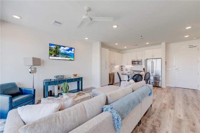 living room with light hardwood / wood-style floors, ceiling fan, and sink