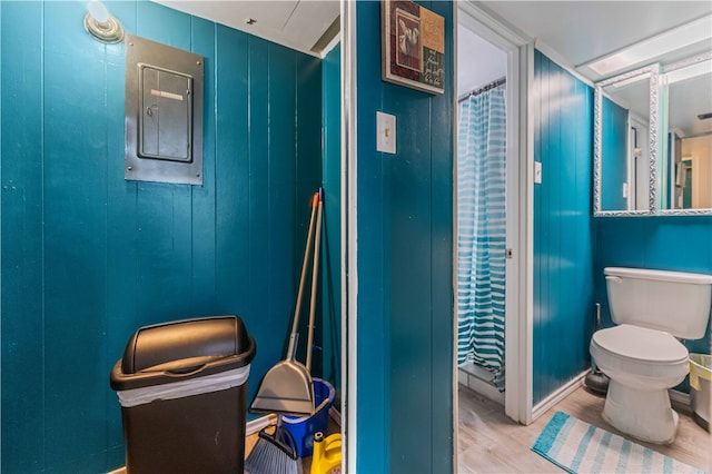 bathroom with electric panel, wood-type flooring, wooden walls, and toilet